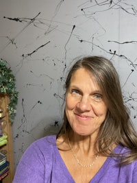 a woman in a purple shirt smiling in front of a wall